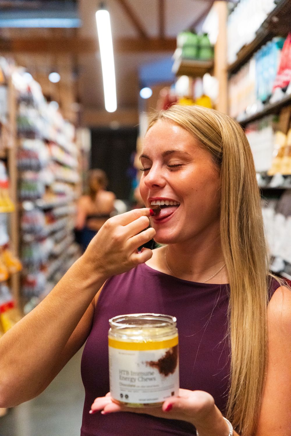 Someone tastes a sample while holding a jar in a grocery store aisle.