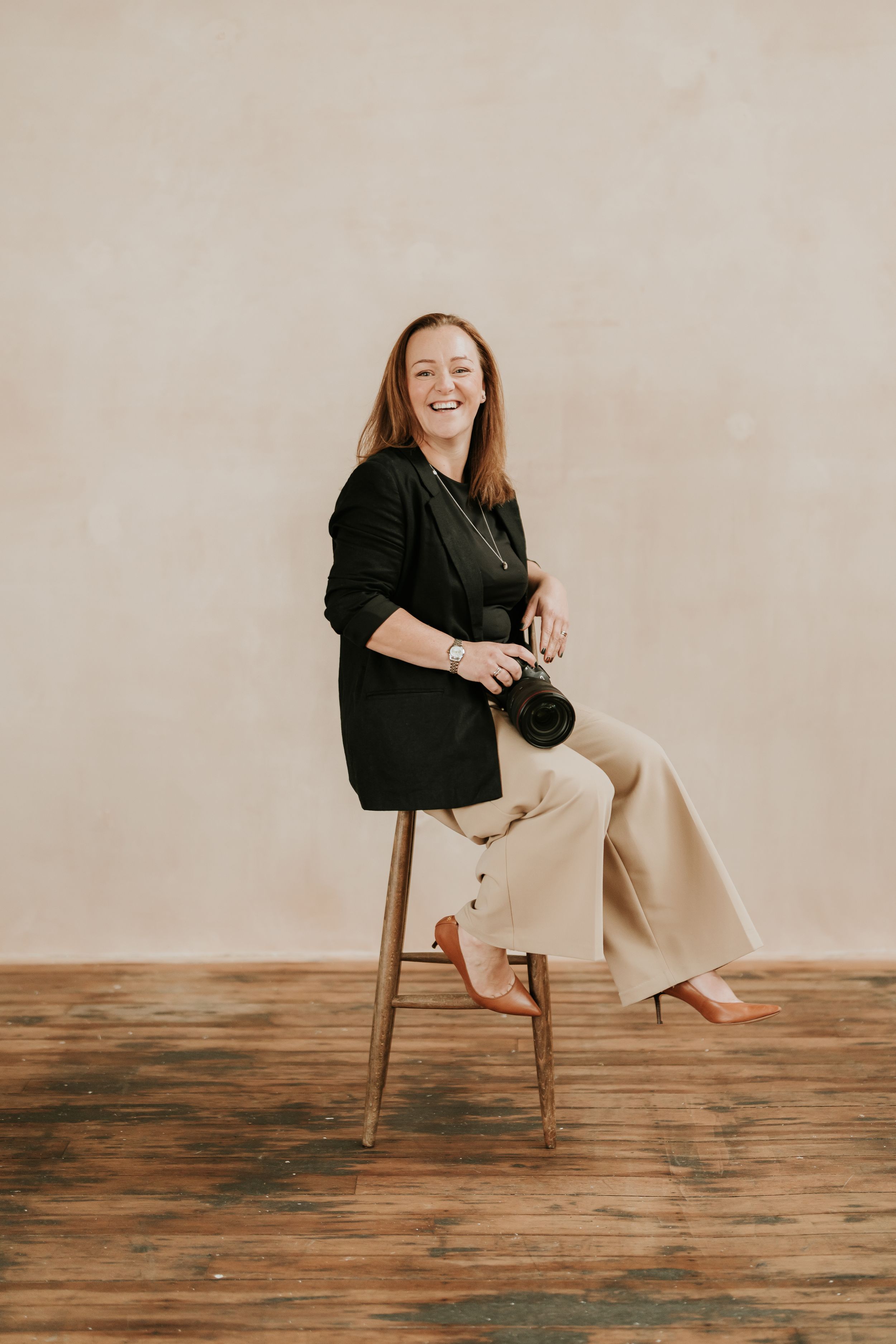 Professional portrait series showing someone in a black blazer sitting casually on a wooden chair against neutral backdrop.