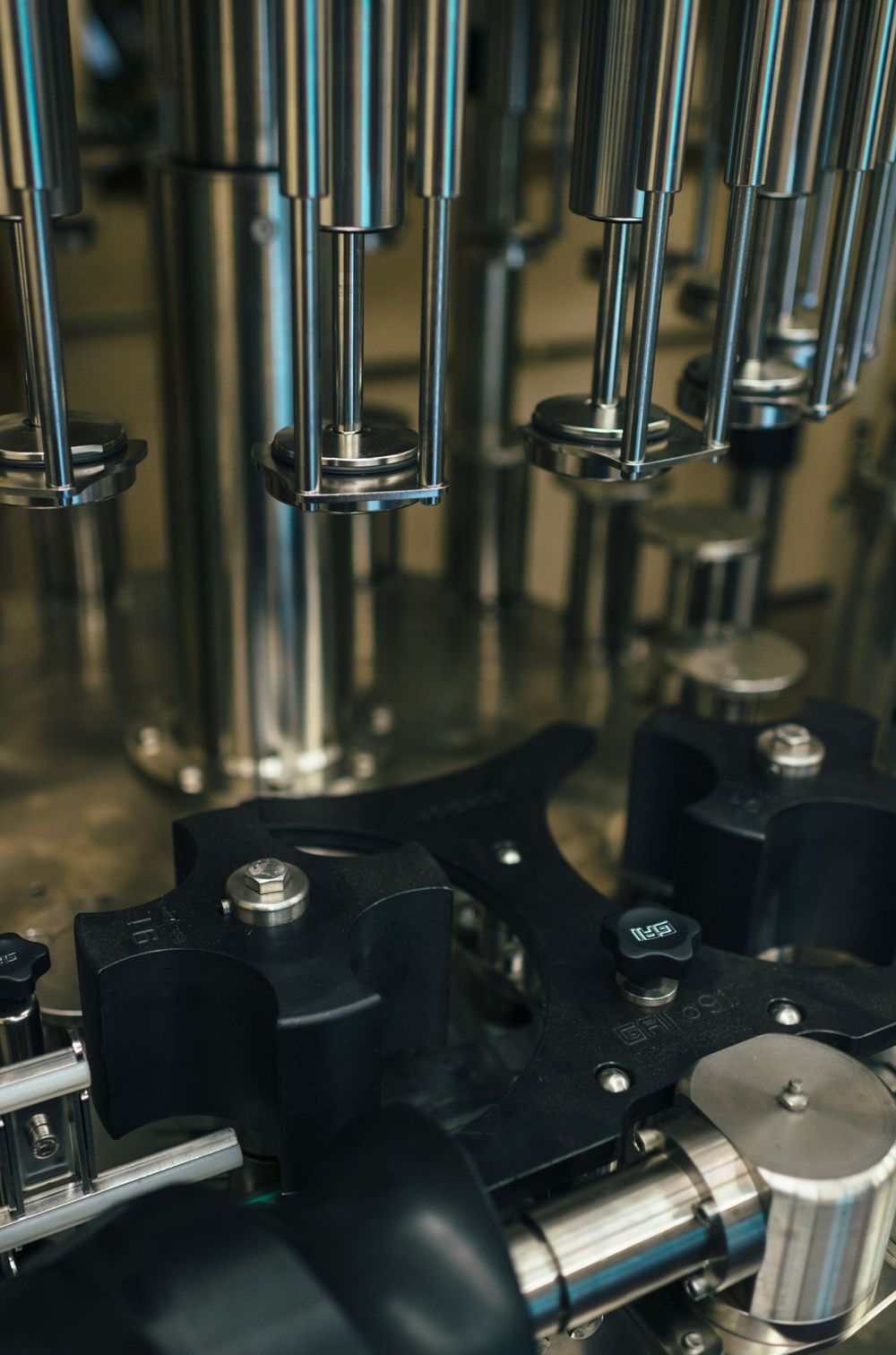Close-up of metallic bottling equipment showing multiple filling nozzles in a row.