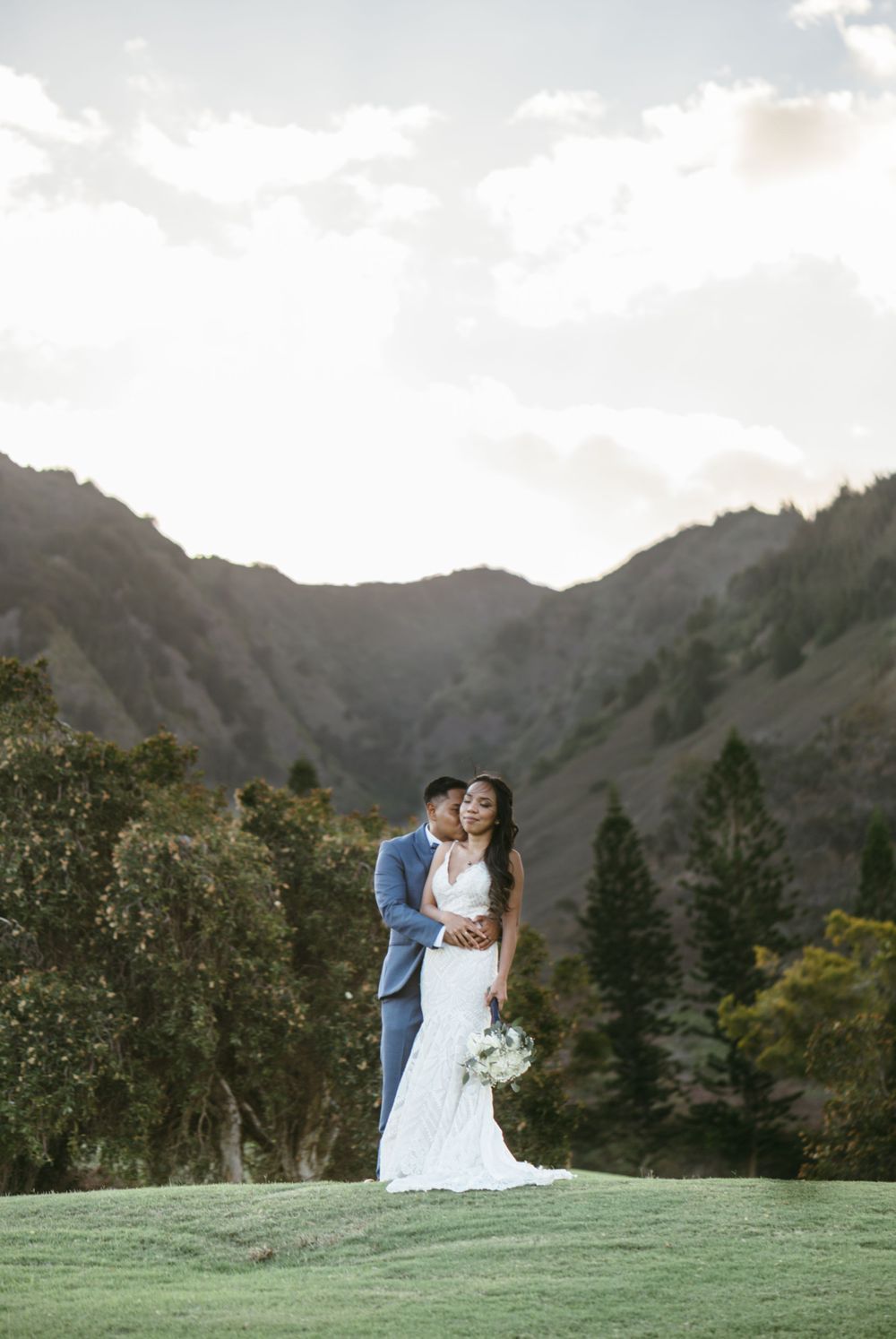 A couple shares a romantic moment on a hilltop with mountains in the background.