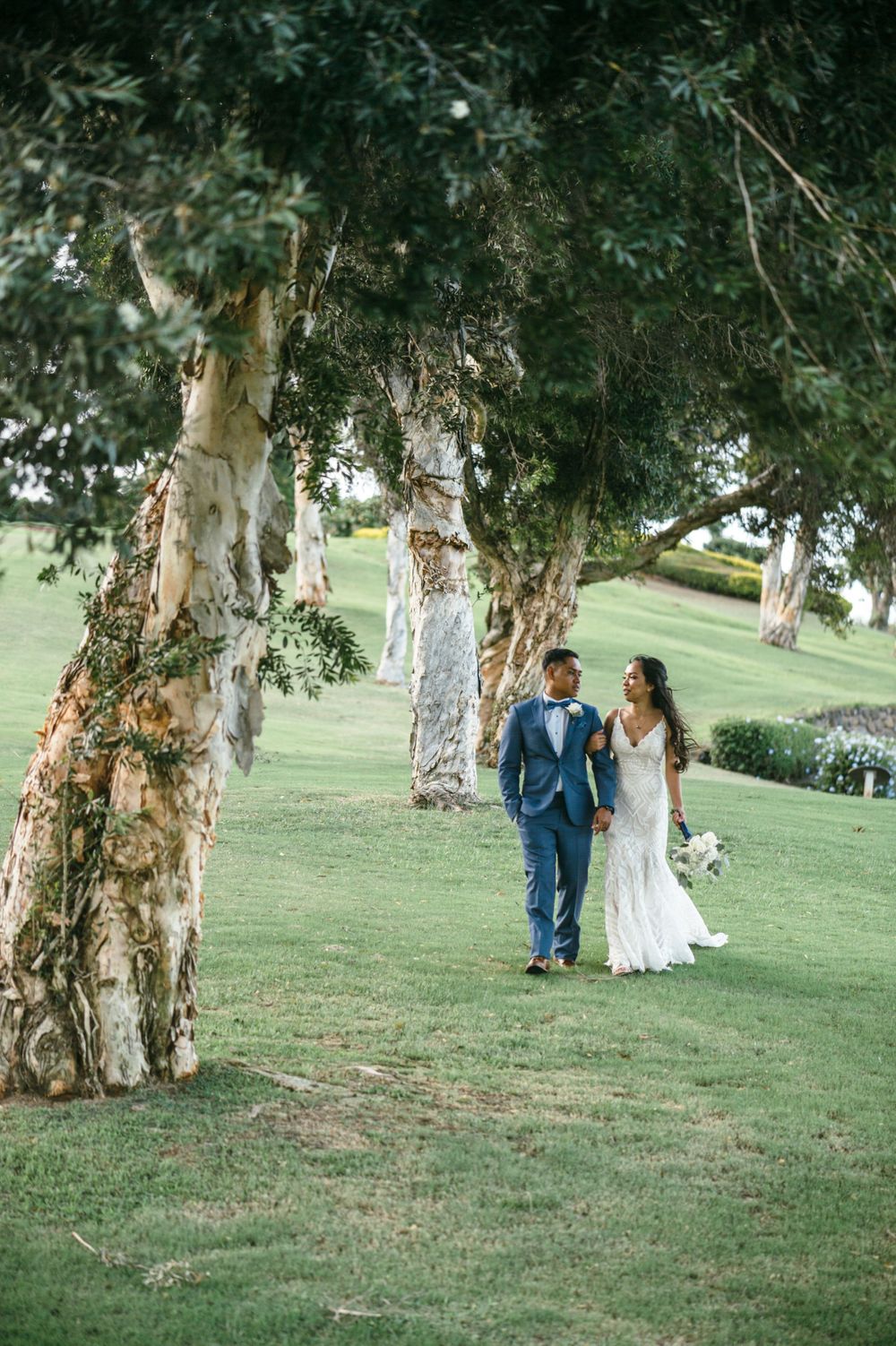 Couple walks under eucalyptus trees on grassy hillside during wedding photoshoot.