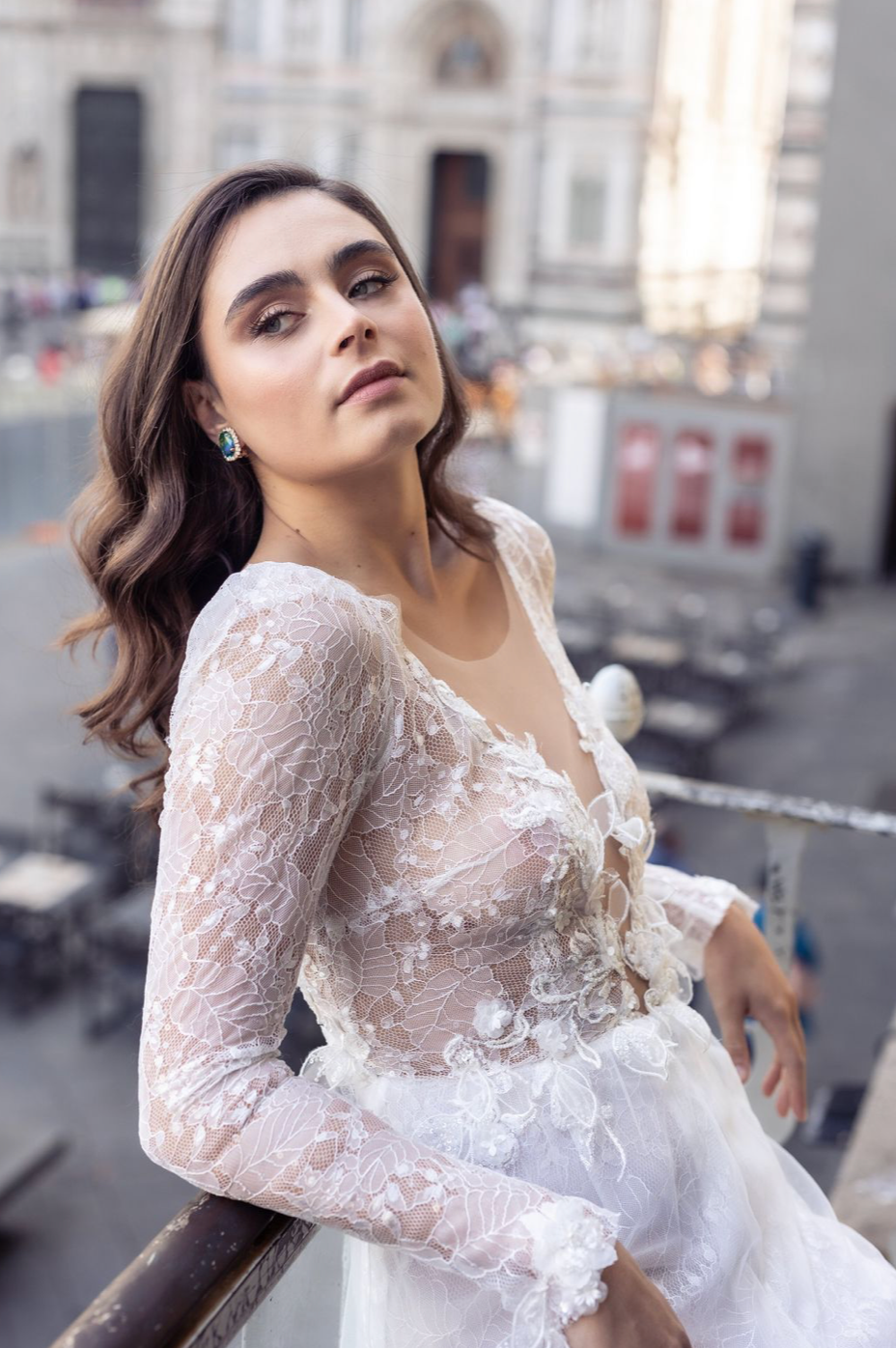 Fashion model wearing white lace long sleeve dress poses elegantly against urban backdrop.