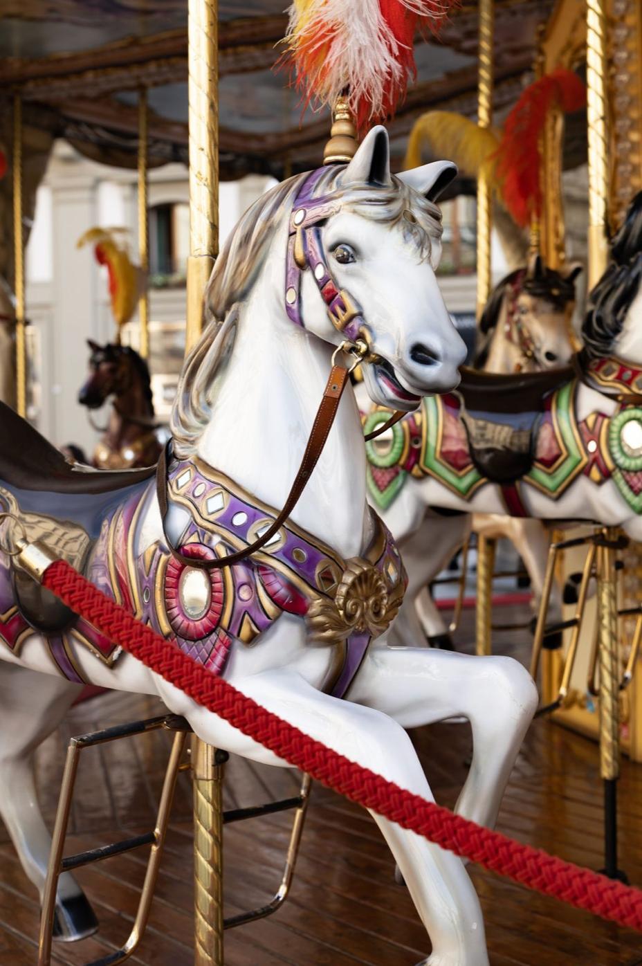 Ornate white carousel horses with red and purple decorative details on traditional fairground merry-go-round poles.
