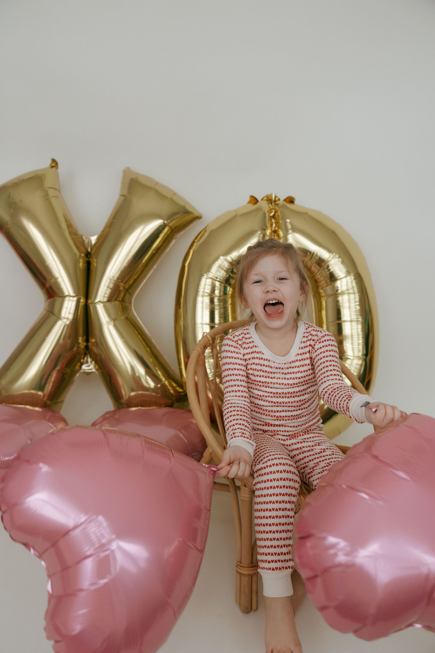 Young children in red and white striped outfits pose playfully with pink and gold balloons against a white backdrop.