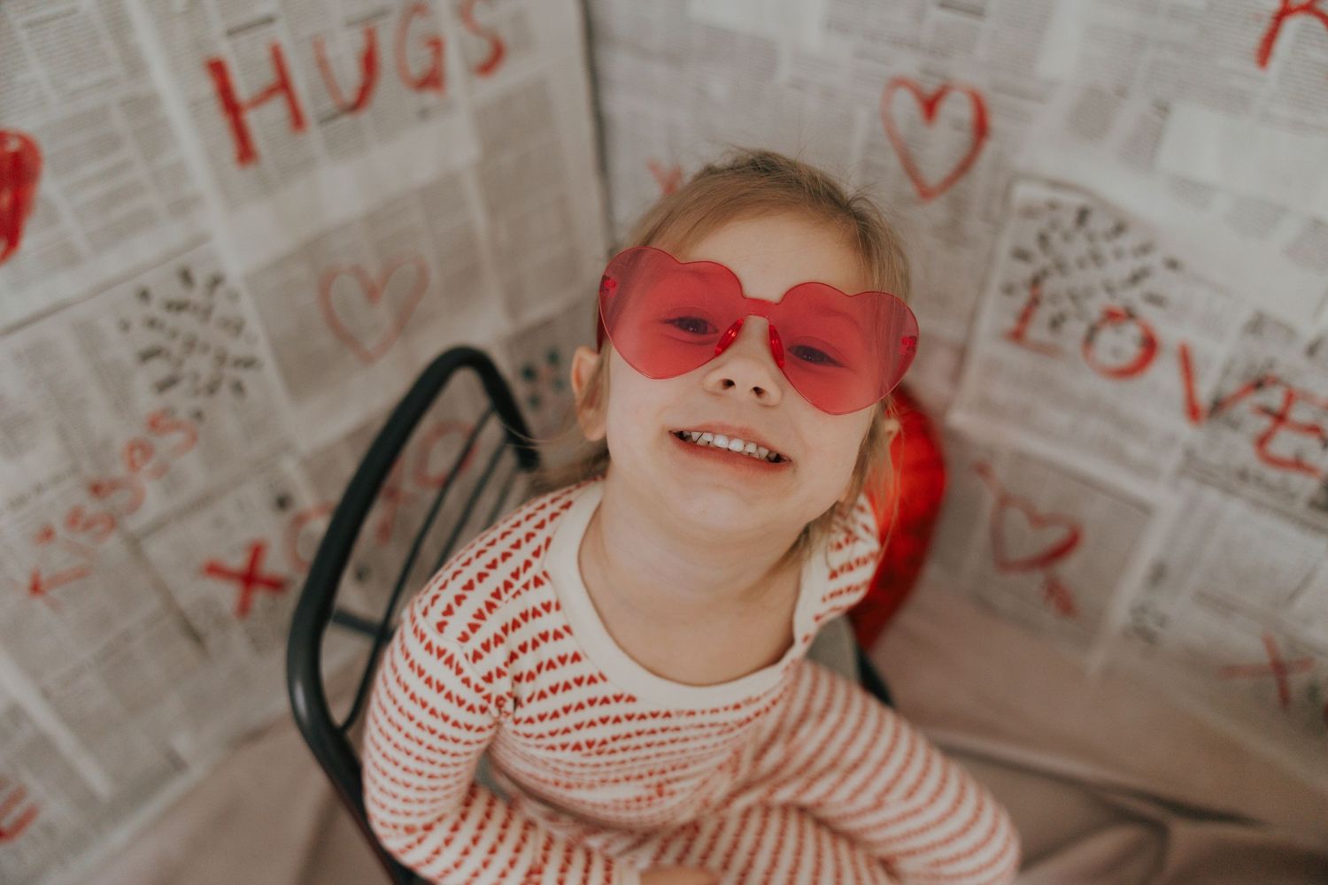 A child wearing red heart-shaped sunglasses and striped shirt poses playfully in a series of candid photos.