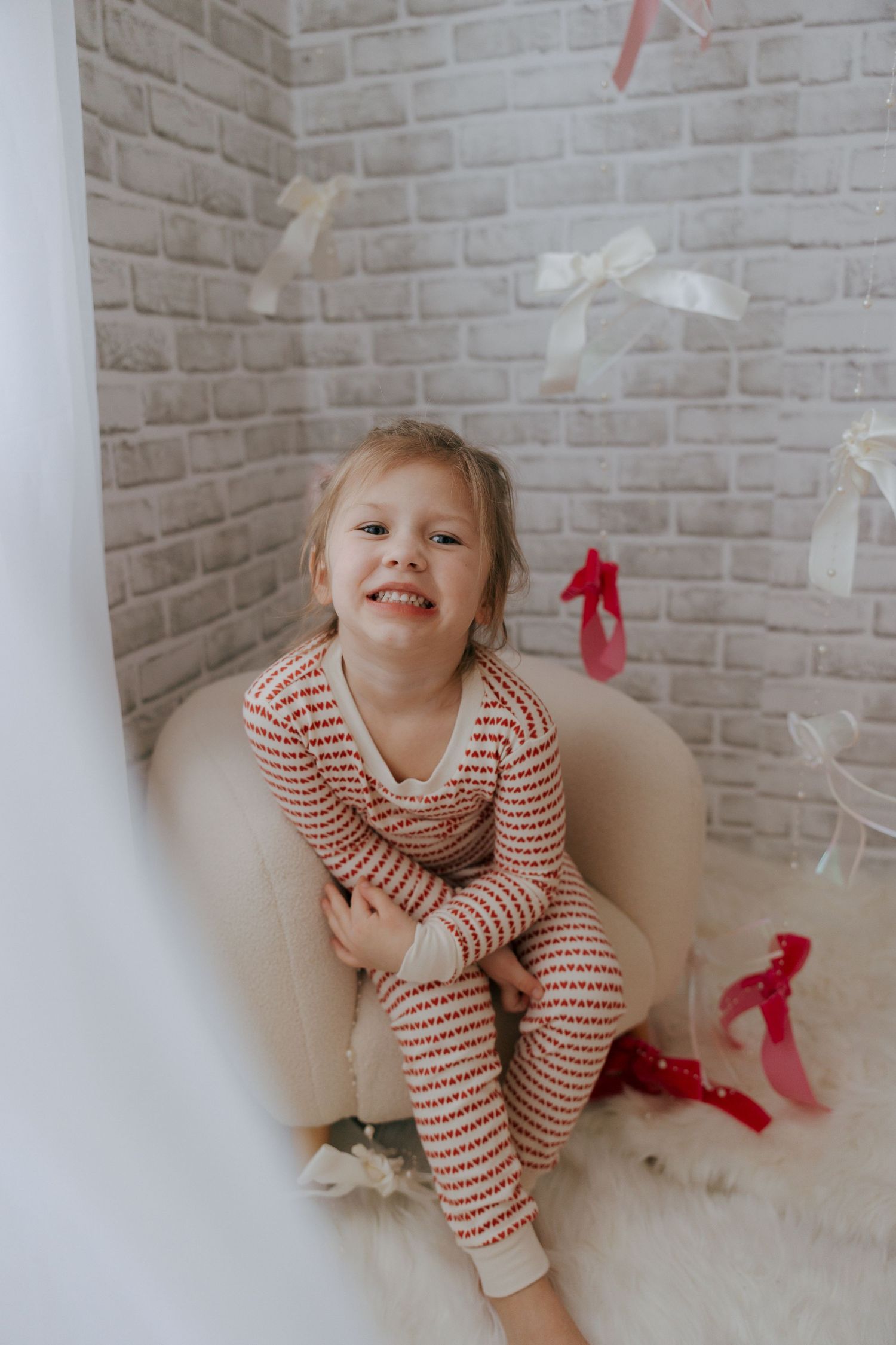 A child in red and white striped pajamas plays on a white floor with festive red bows scattered around.