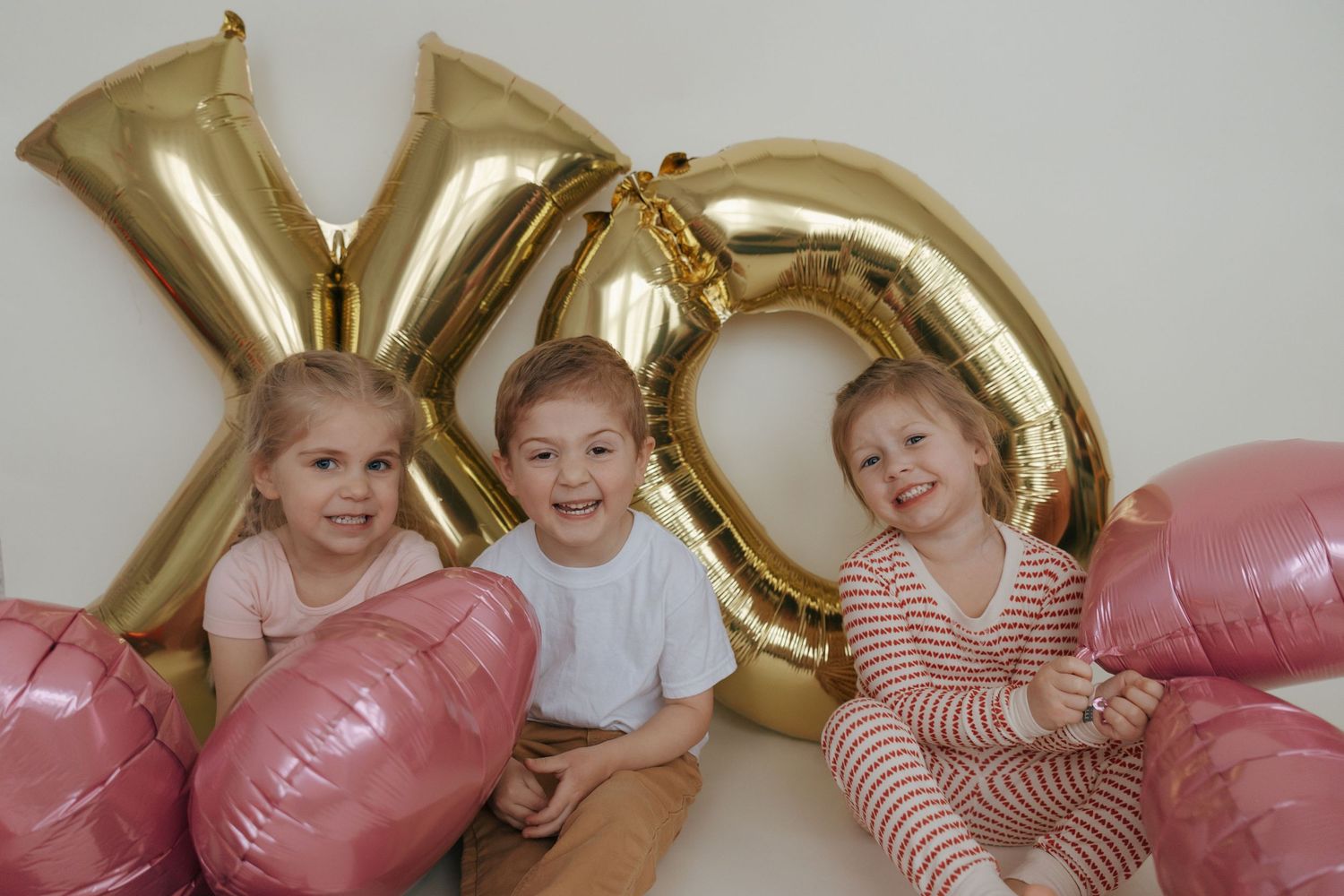 Children playing and laughing beneath large gold balloon letters and pink balloons at a celebration.