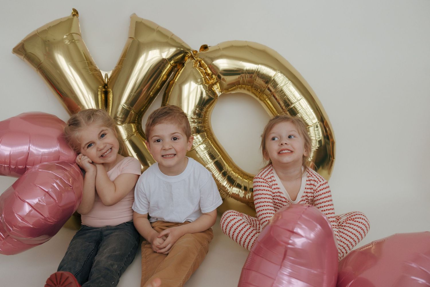 Valentine's Day themed photo setup with pink and gold balloon decorations against a white wall.