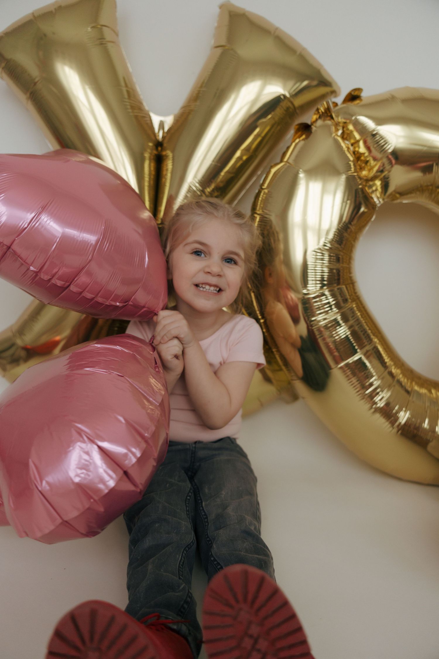 A child lies on the floor surrounded by pink and gold balloon decorations for a celebration.
