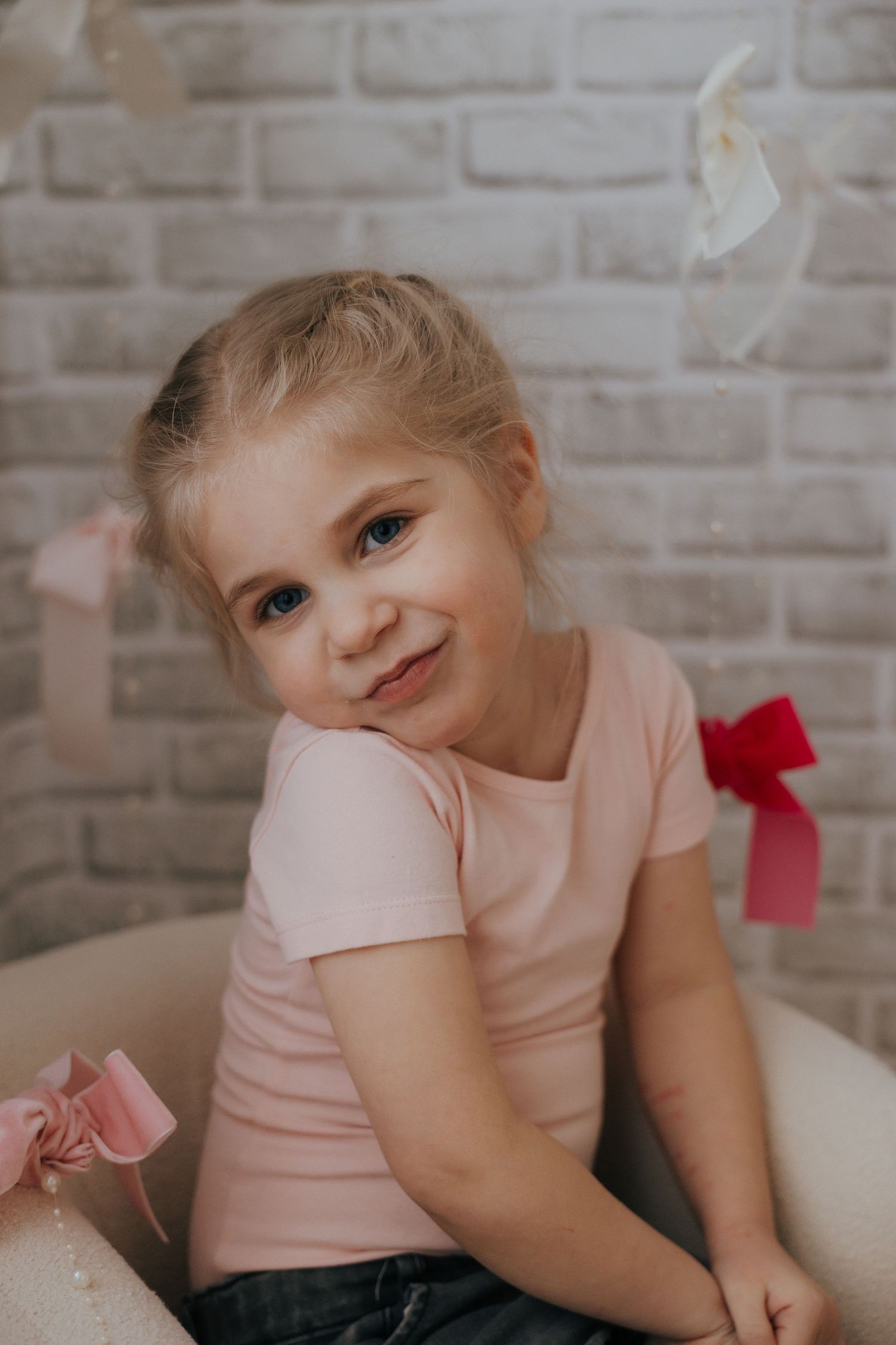 A child in a pink shirt poses playfully against a light brick wall background.