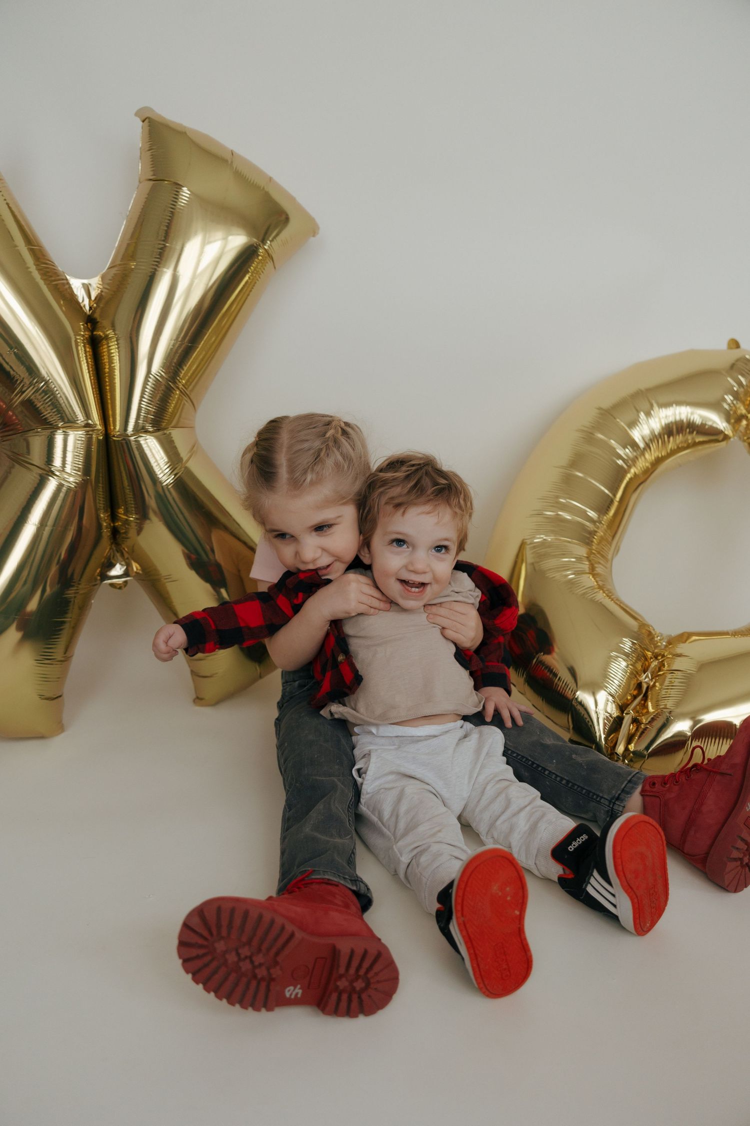 Four connected photos show a baby lying on the floor next to gold letter balloons in a festive holiday setting.
