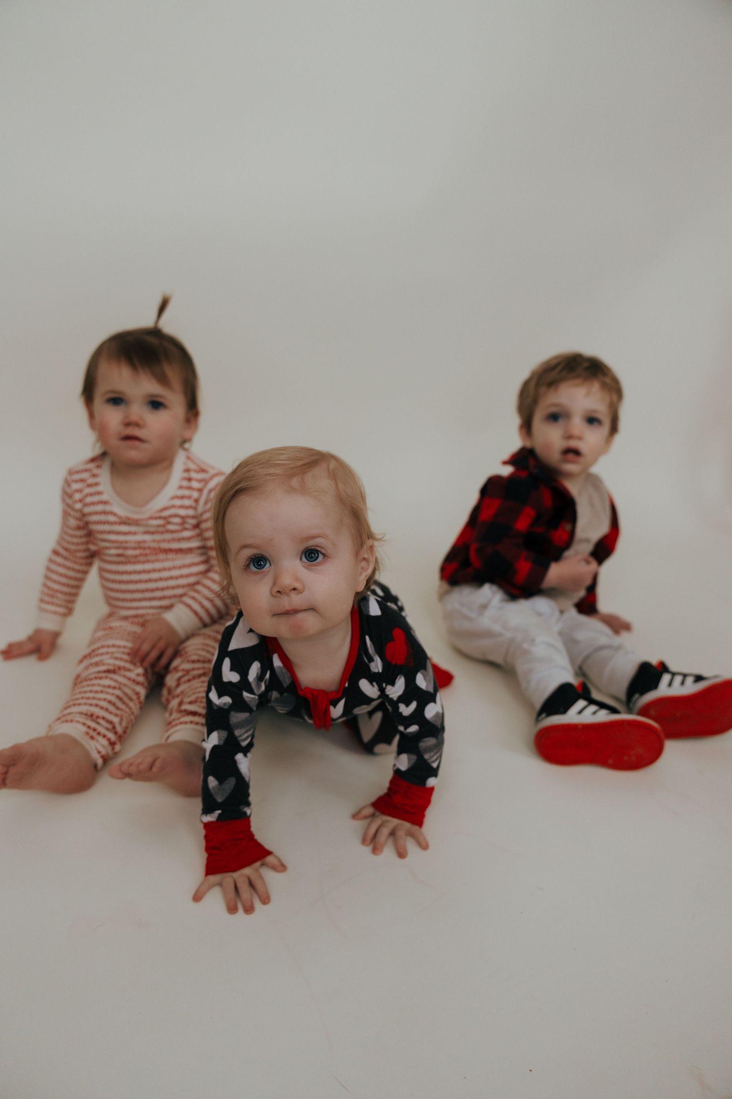 Three young children in casual outfits sit on a white floor during a photo session.