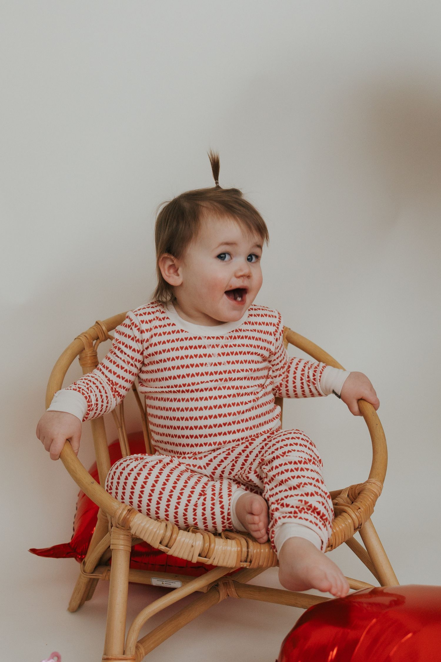 Baby in red and white striped outfit lounges in vintage rattan chair showing different playful poses.