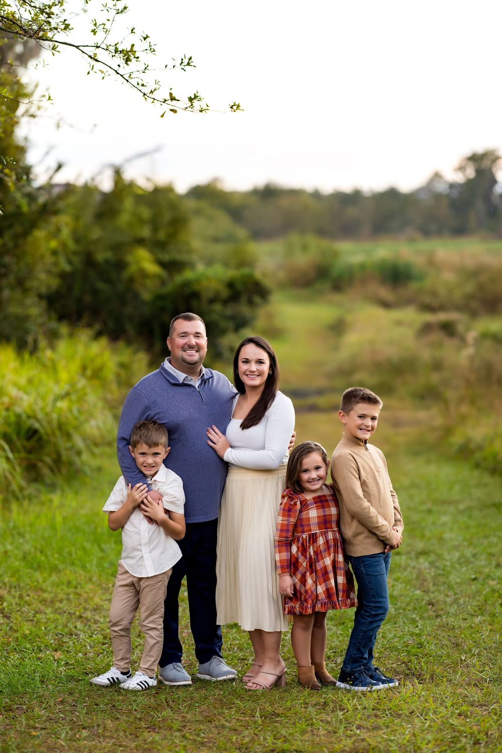 Family standing together in a grassy field during an outdoor autumn photo session.
