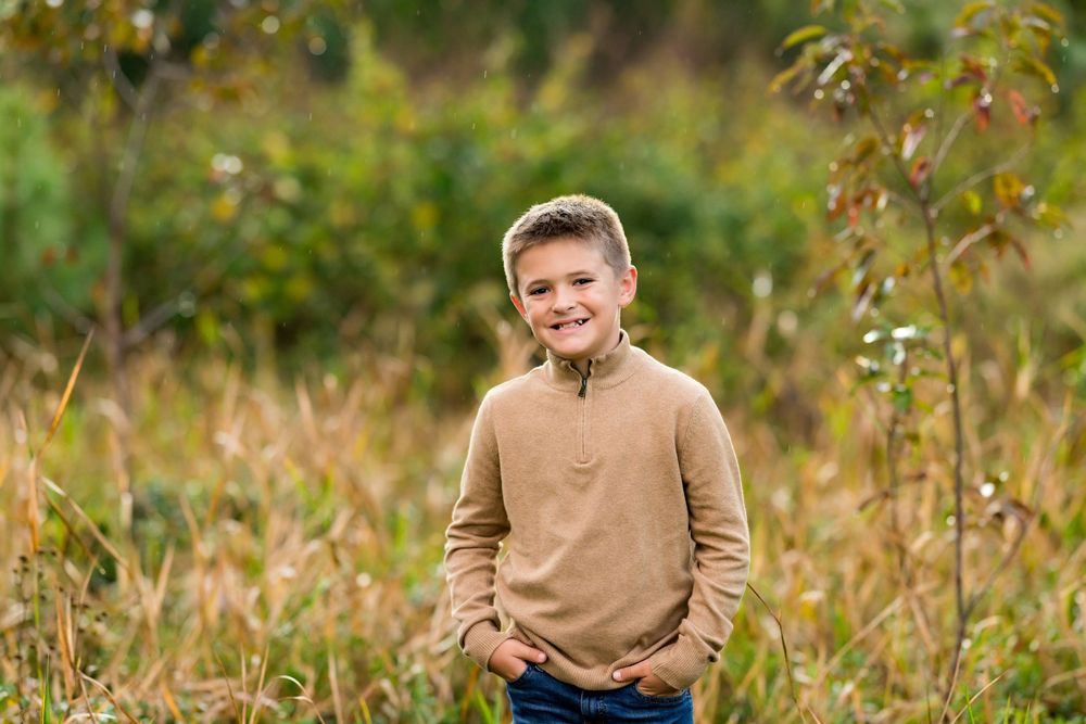 Someone wearing a beige sweater poses outdoors in a natural setting with tall grass and greenery in the background.