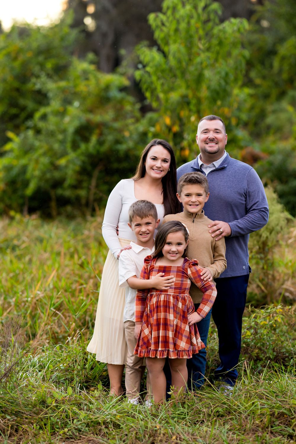 Family of five poses together outdoors in casual attire against a green natural background.