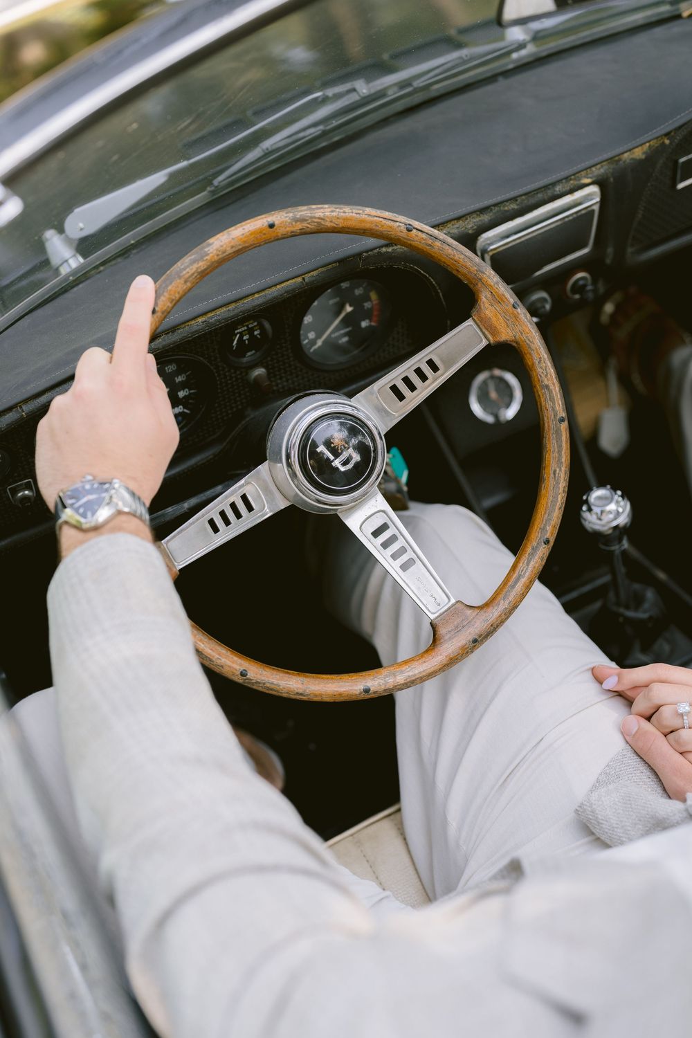 Person in white sweater demonstrates various hand positions on a vintage wooden steering wheel in a classic car interior.