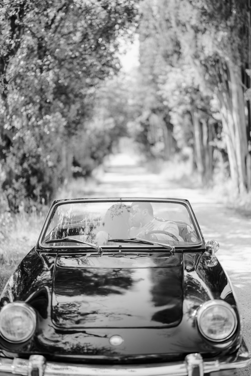 Black vintage Porsche sports car photographed from multiple angles on a tree-lined road in monochrome style.