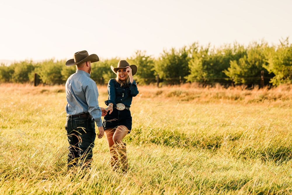 A couple walks through a sunlit meadow of tall golden grass during sunset creating a romantic silhouette.