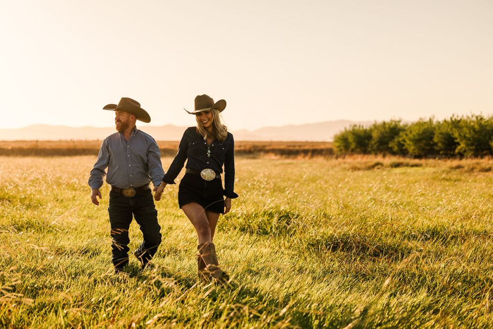 Two silhouetted figures walk through a golden wheat field at sunset creating a peaceful rural scene.