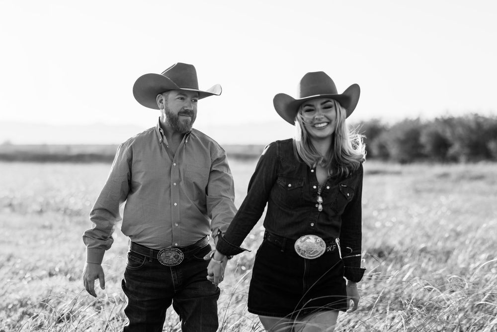A black and white photo of a couple riding horses through a grassy field together.