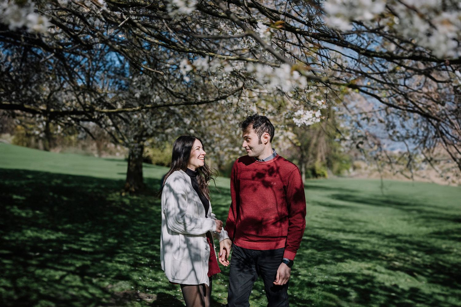 Coppia che sorride durante uno shooting fotografico sotto i ciliegi in fiore in un giardino primaverile