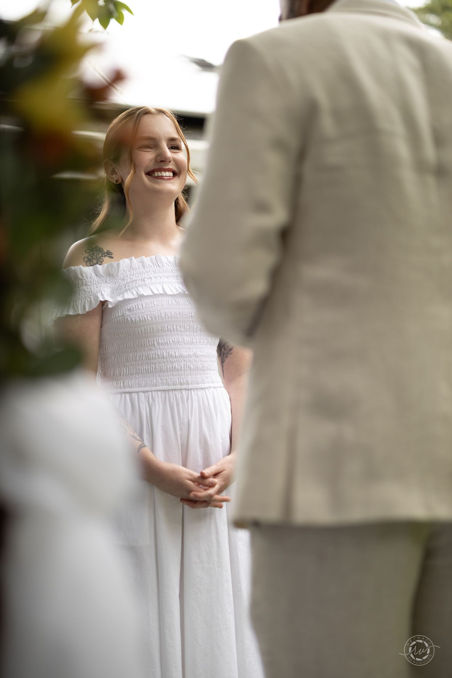 A young person in a white dress laughs joyfully during an outdoor photoshoot.