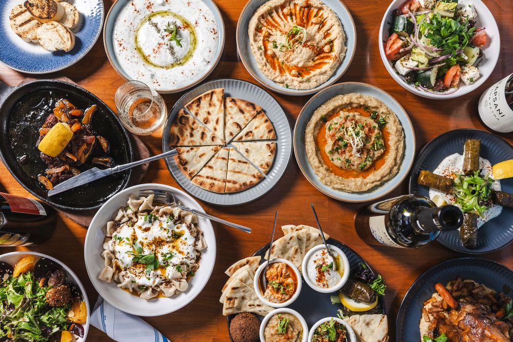Overhead view of a Mediterranean restaurant table filled with hummus, pita bread, salads and various mezze dishes.