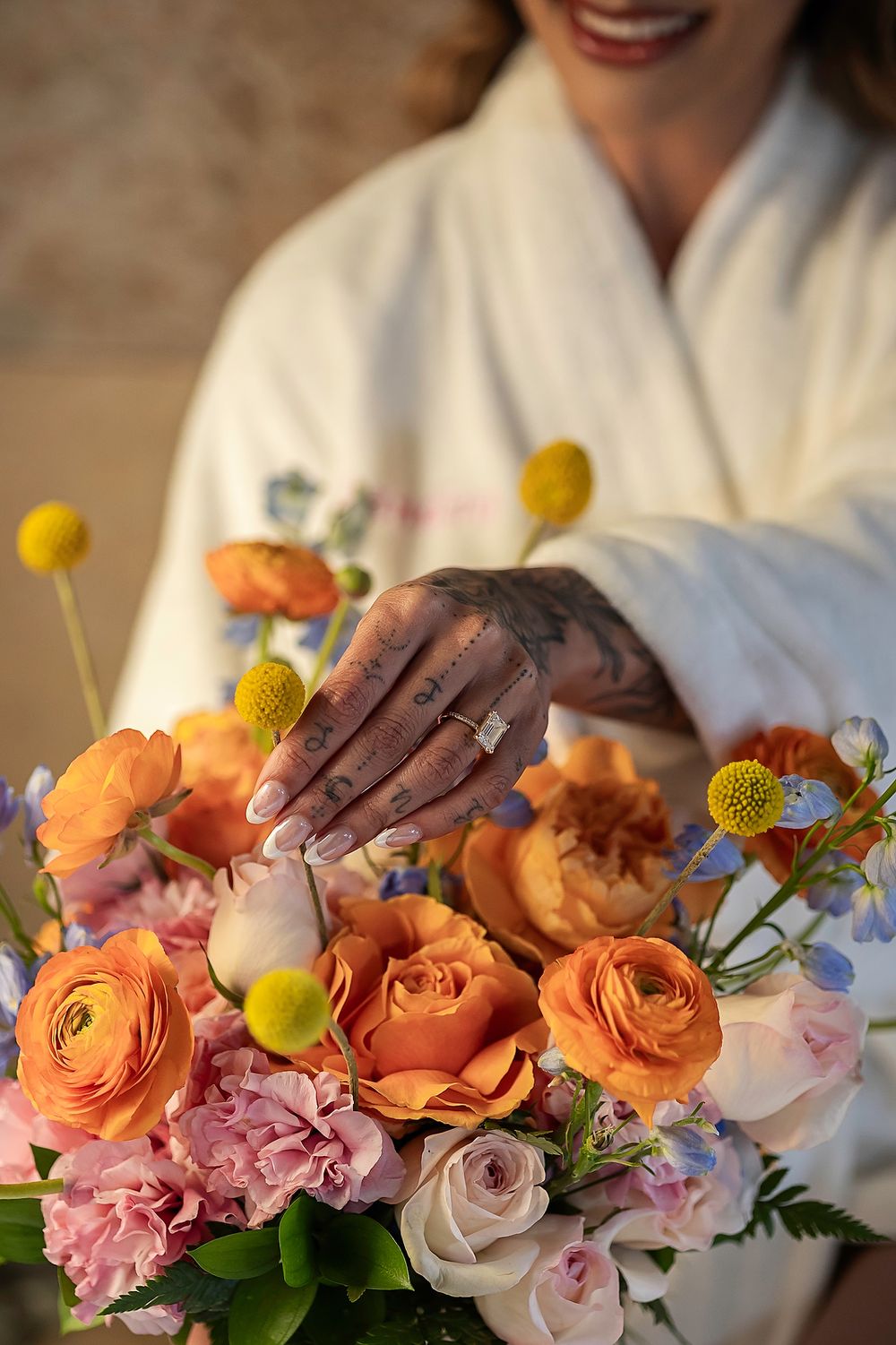 Florist arranges vibrant orange ranunculus, pink orchids and yellow craspedia flowers in a delicate spring arrangement.