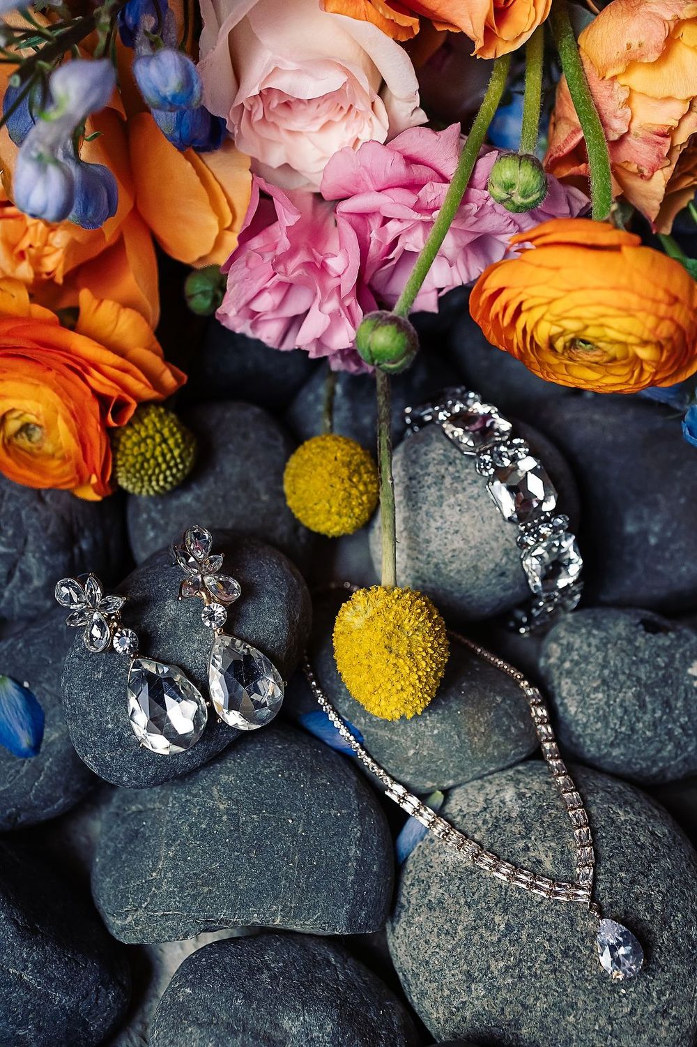 Colorful wedding flowers with orange and pink blooms arranged with yellow craspedia and stones on dark surface.