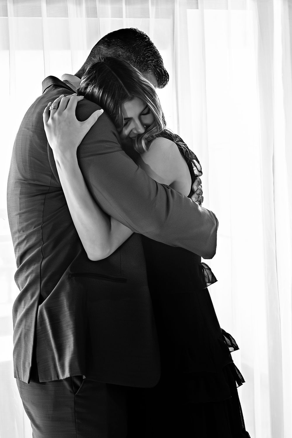 Black and white photo of a tender embrace between two people sharing an intimate moment by a window.
