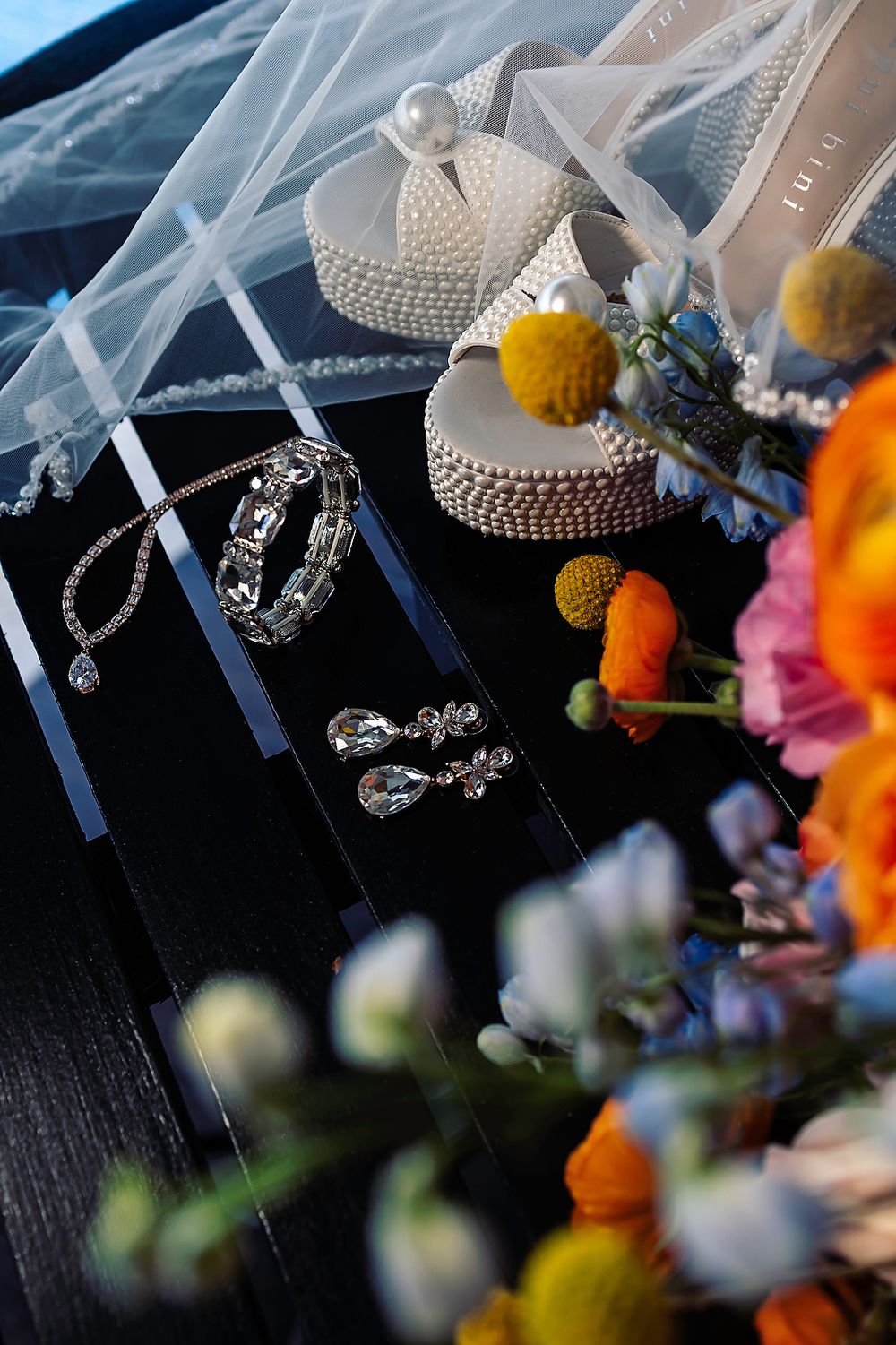 Wedding jewelry and accessories including a pearl-studded headpiece and floral details arranged on a dark surface.