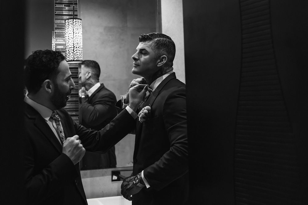 Black and white candid photo of groomsmen getting ready in a dimly lit room.