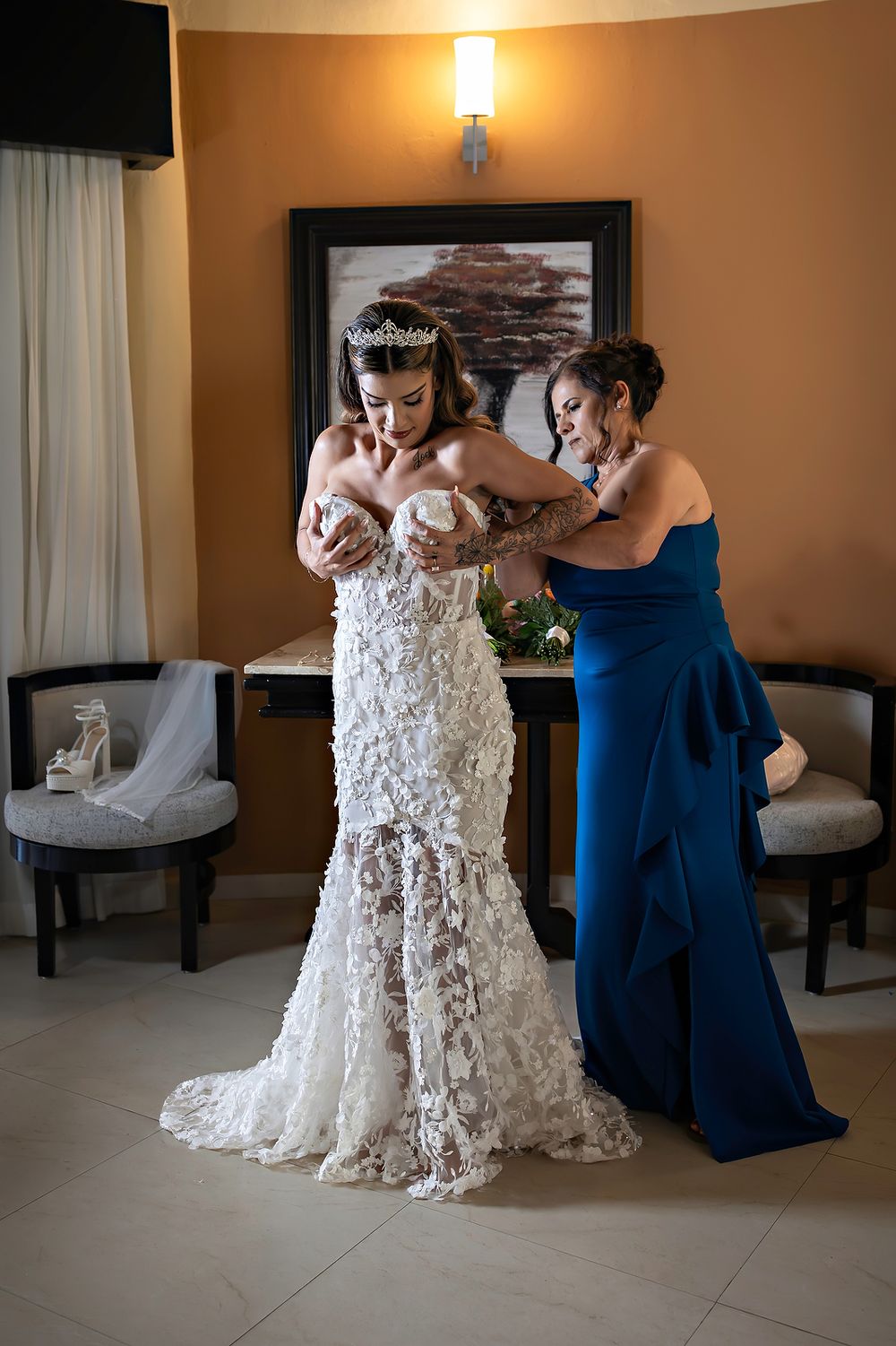 Wedding preparations showing attendants helping adjust an intricate lace wedding dress.