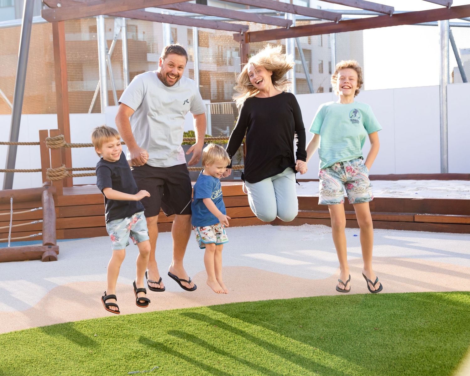 Children playing and running on artificial turf in an indoor recreational space with natural lighting.