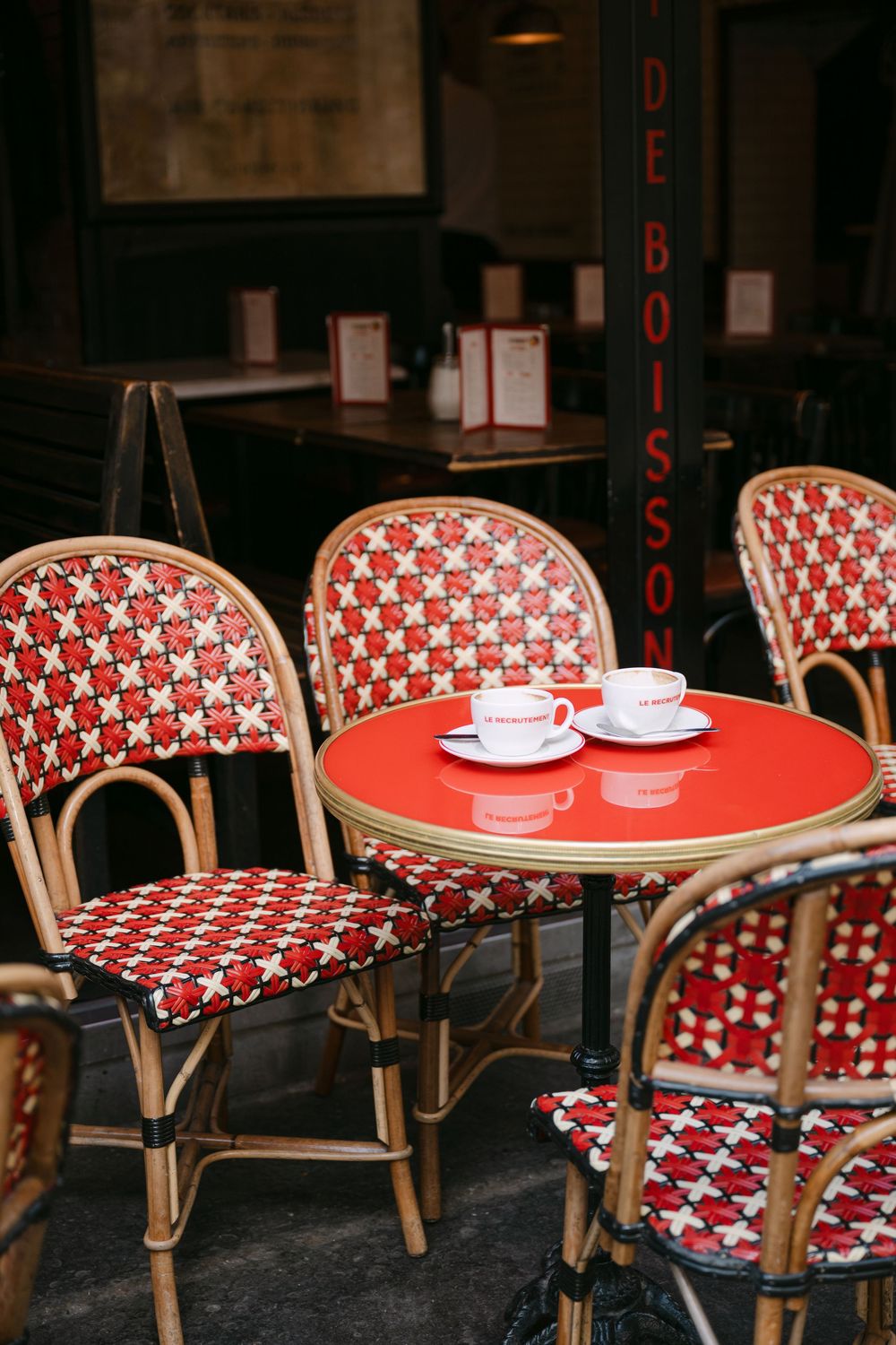 Empty red and white bistro chairs and tables at a traditional Parisian sidewalk cafe.
