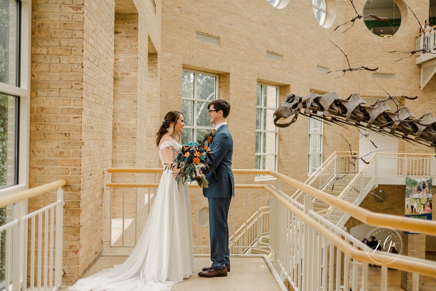 Couple shares a romantic first look moment in a sunlit brick atrium with white architectural details.