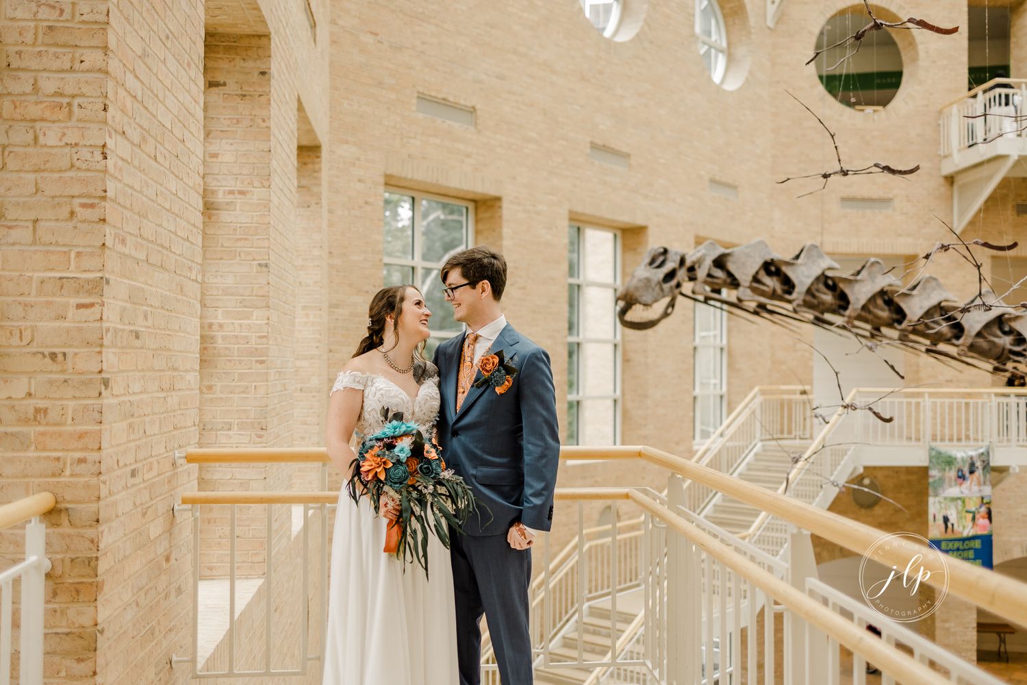 Wedding couple stands together in a bright architectural space with brick walls.