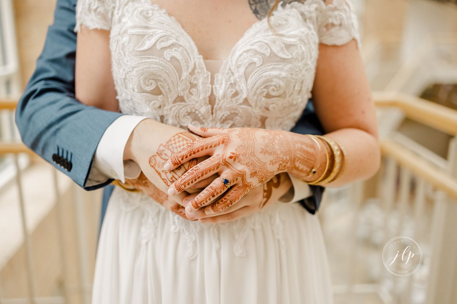 Close-up detail of lace wedding dress bodice and hands in an indoor setting.