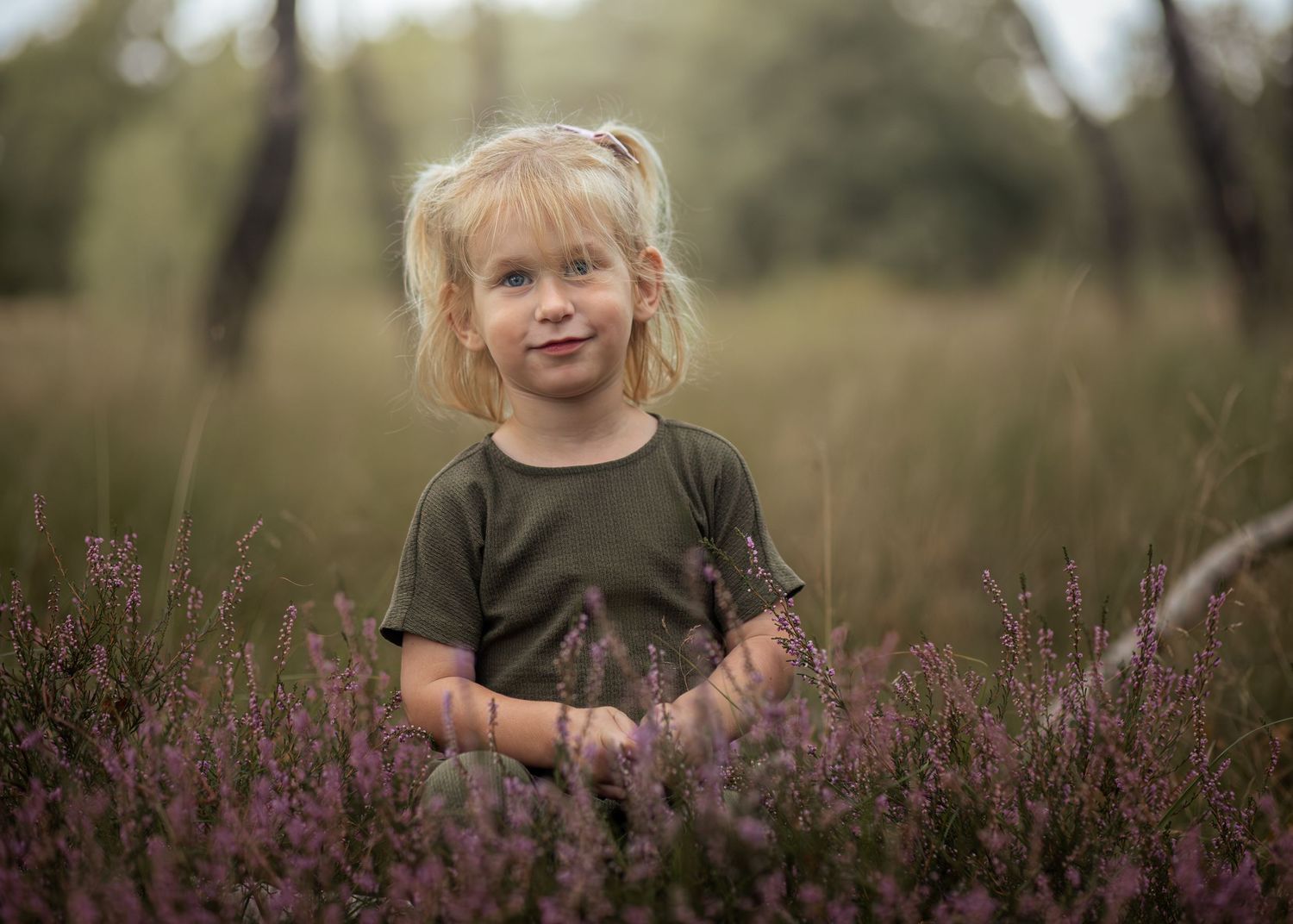 Foto van peuter tussen heide in het bos kijkend naar camera.