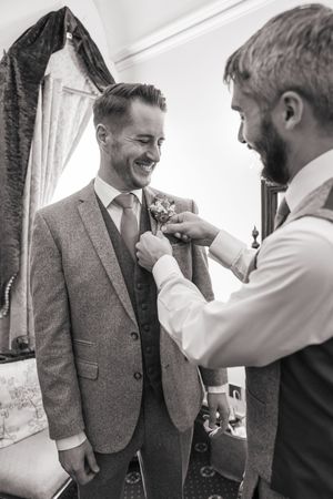 Groomsmen help adjust the groom's tie and suit before the wedding ceremony.