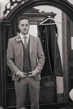 Five black and white portraits show a man in vintage tweed suits standing by ornate doorways in varying poses.