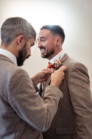 A sequence showing someone adjusting a boutonniere on another person's brown tweed suit jacket.