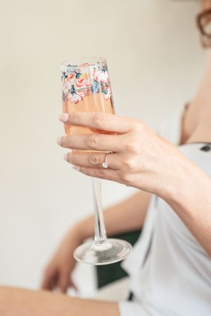 Hand holding a champagne flute with floral design showing engagement ring.