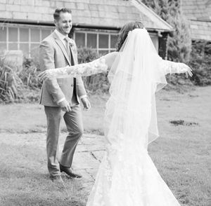 Bride in flowing white dress twirls joyfully in outdoor garden setting creating ethereal movement in black and white photo.