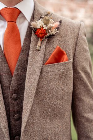 Brown tweed groomsmen suits with orange ties and small floral boutonnieres.
