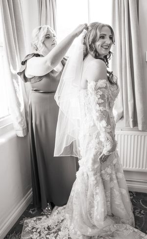 Getting ready scenes show a flowing white lace wedding gown against light-filled windows and curtains.