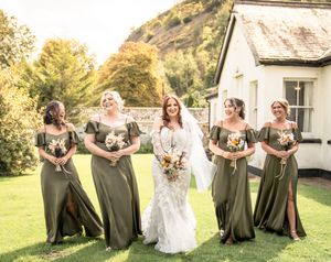 Wedding party poses playfully on grass with bride and bridesmaids in olive green dresses.