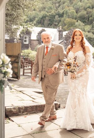 People celebrate at an outdoor wedding venue with stone walls and rustic decor on a sunny day.