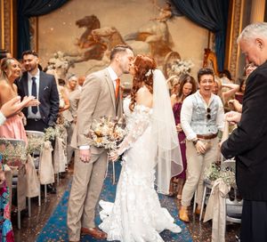 Wedding guests toss flower petals and celebrate as newlyweds exit their ceremony down an aisle.